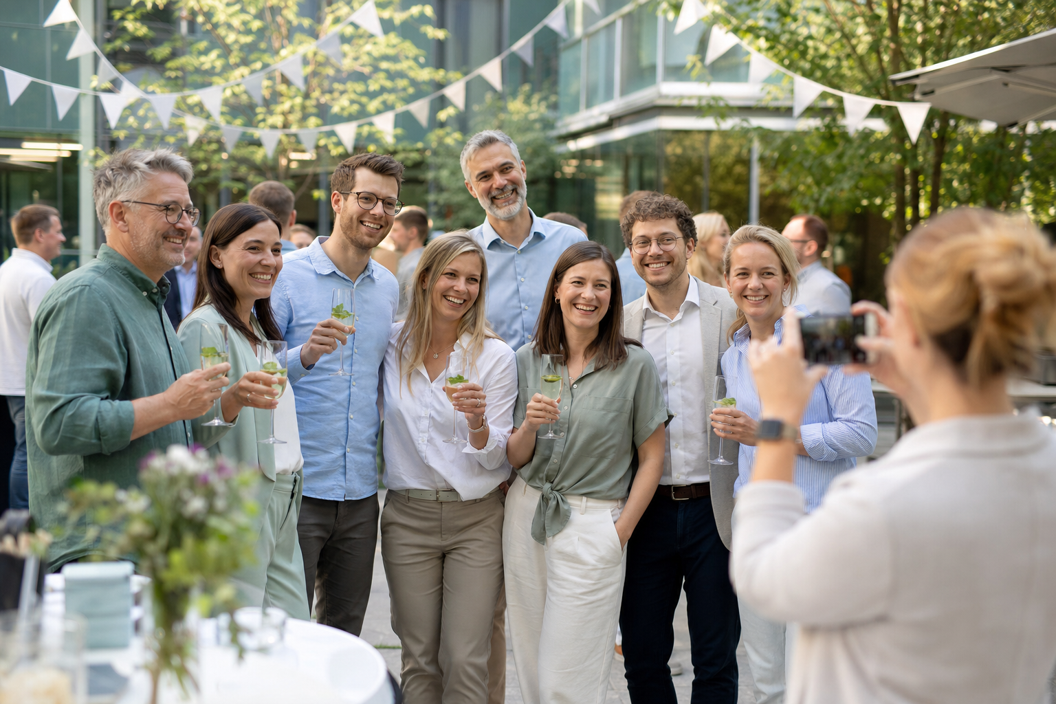Ein Team feiert gemeinsam in einem hellen begrünten Bürohof und macht ein Gruppenfoto